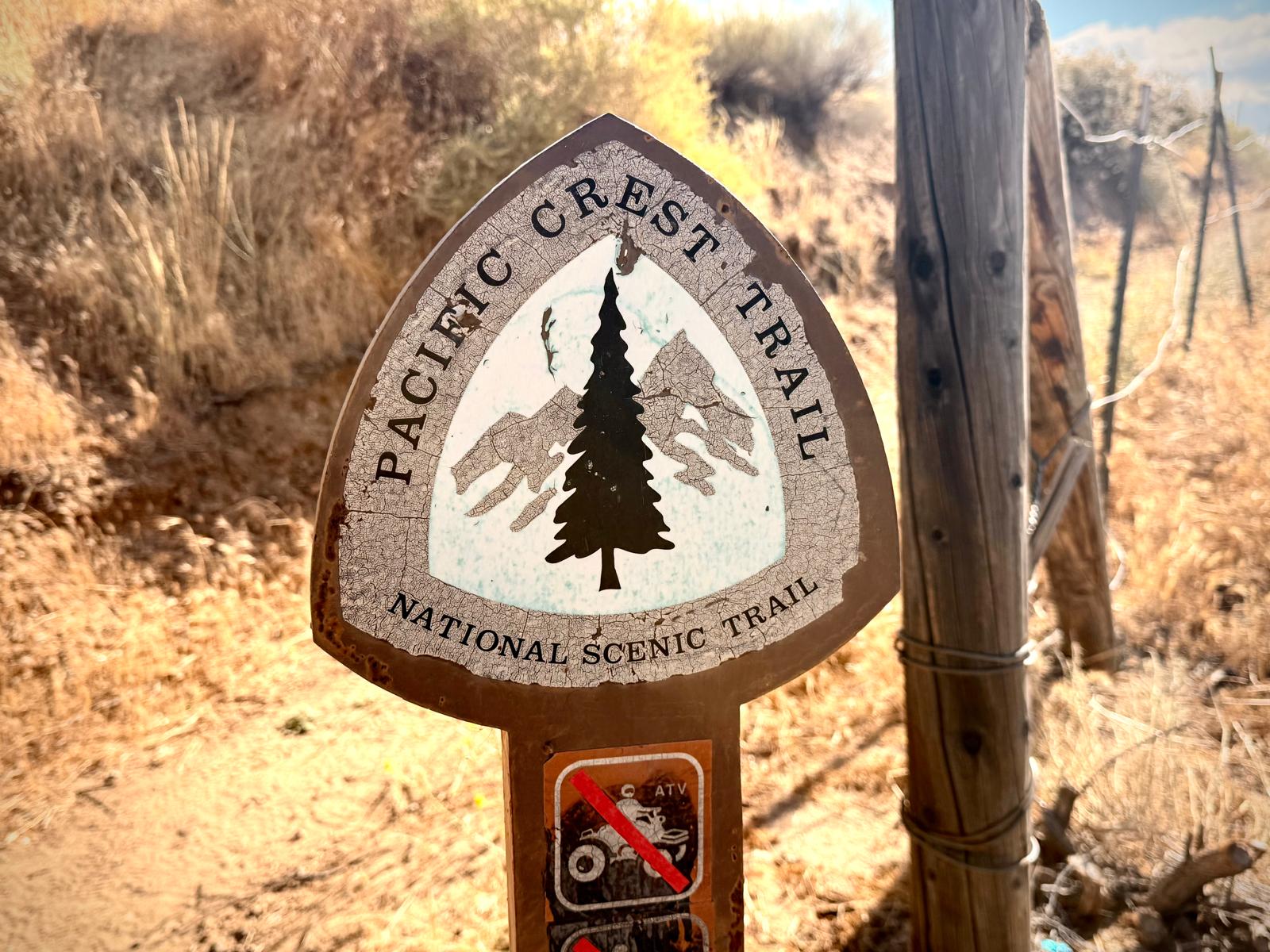 A weathered Pacific Crest Trail marker in hard sun
