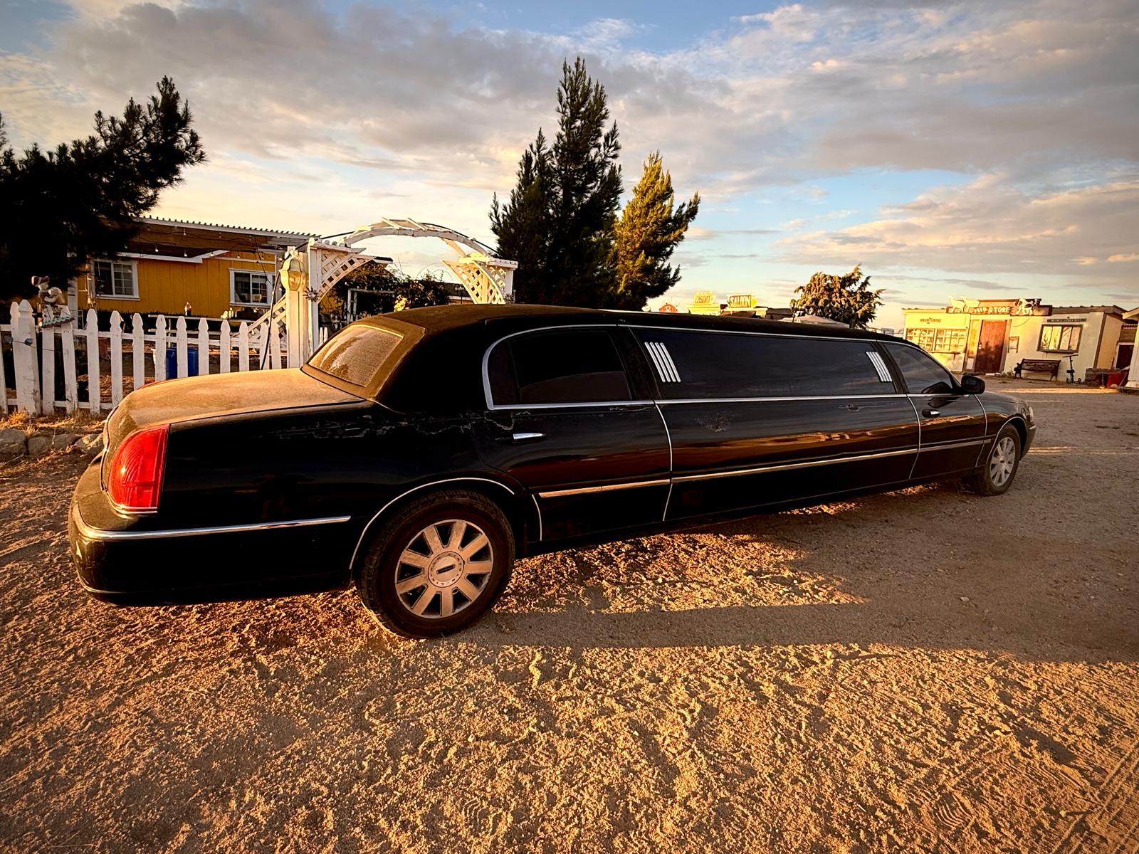 The black stretch limousine parked on the dirt at golden hour